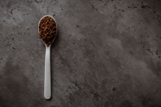One spoonful of instant granulated coffee isolated on a dark kitchen counter. Top view flat lay with empty space for text on the right