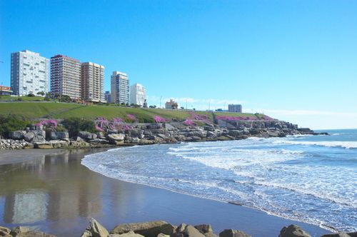 Free Beautiful beachfront view of Mar del Plata with skyline. Waves crashing on the shore under a clear blue sky. Stock Photo