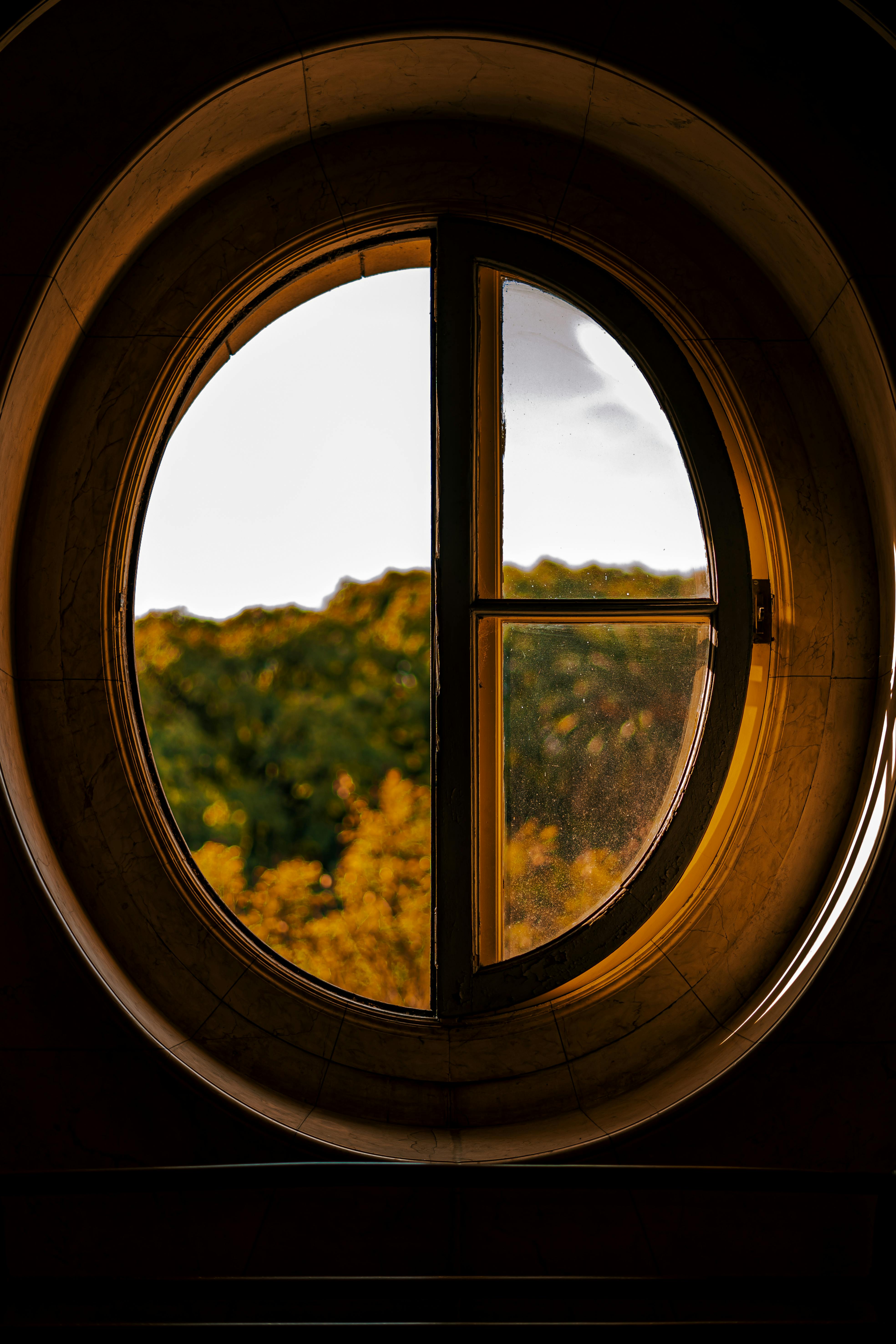A serene landscape captured through an oval glass window indoors.