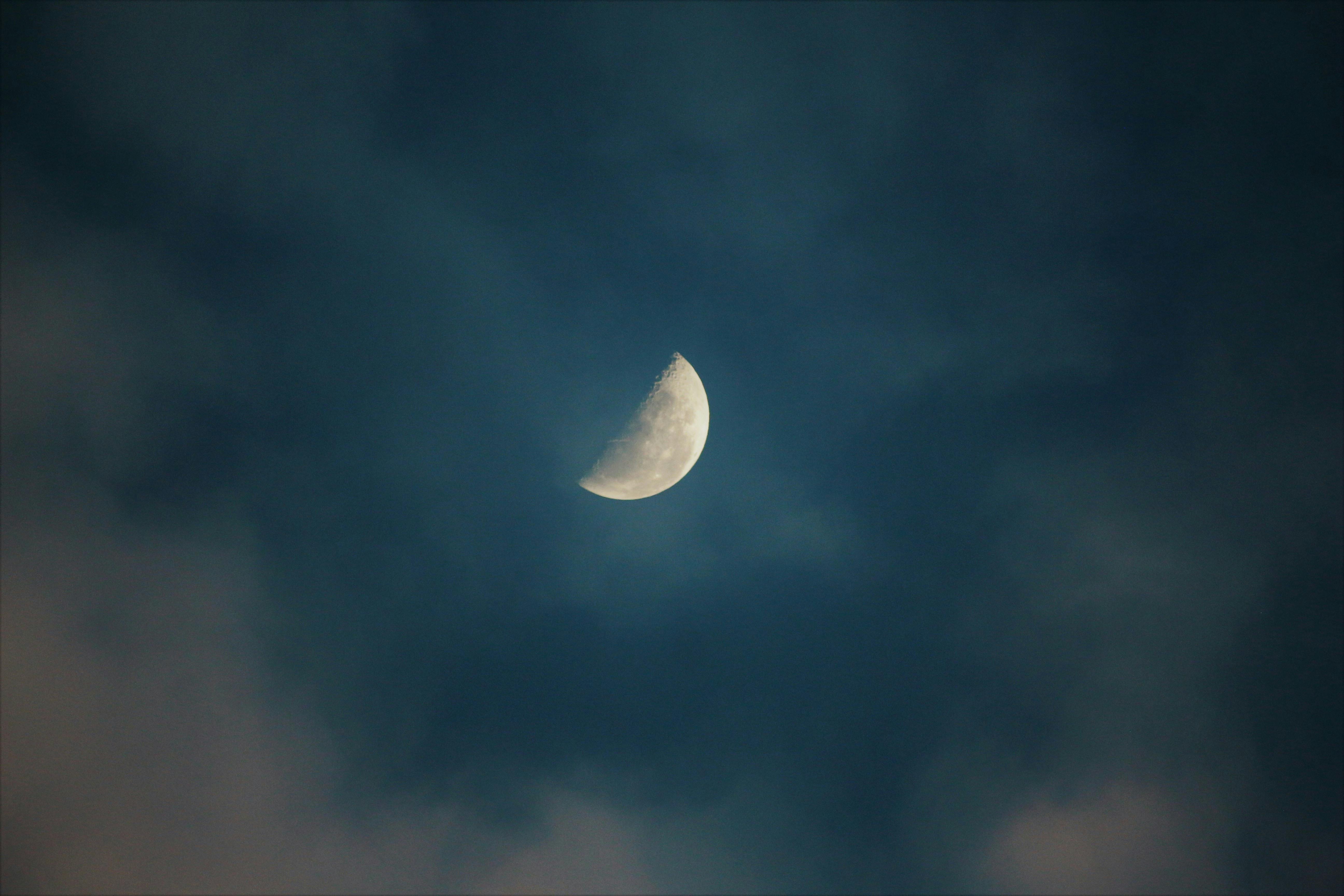A serene view of the half moon surrounded by clouds in the night sky.