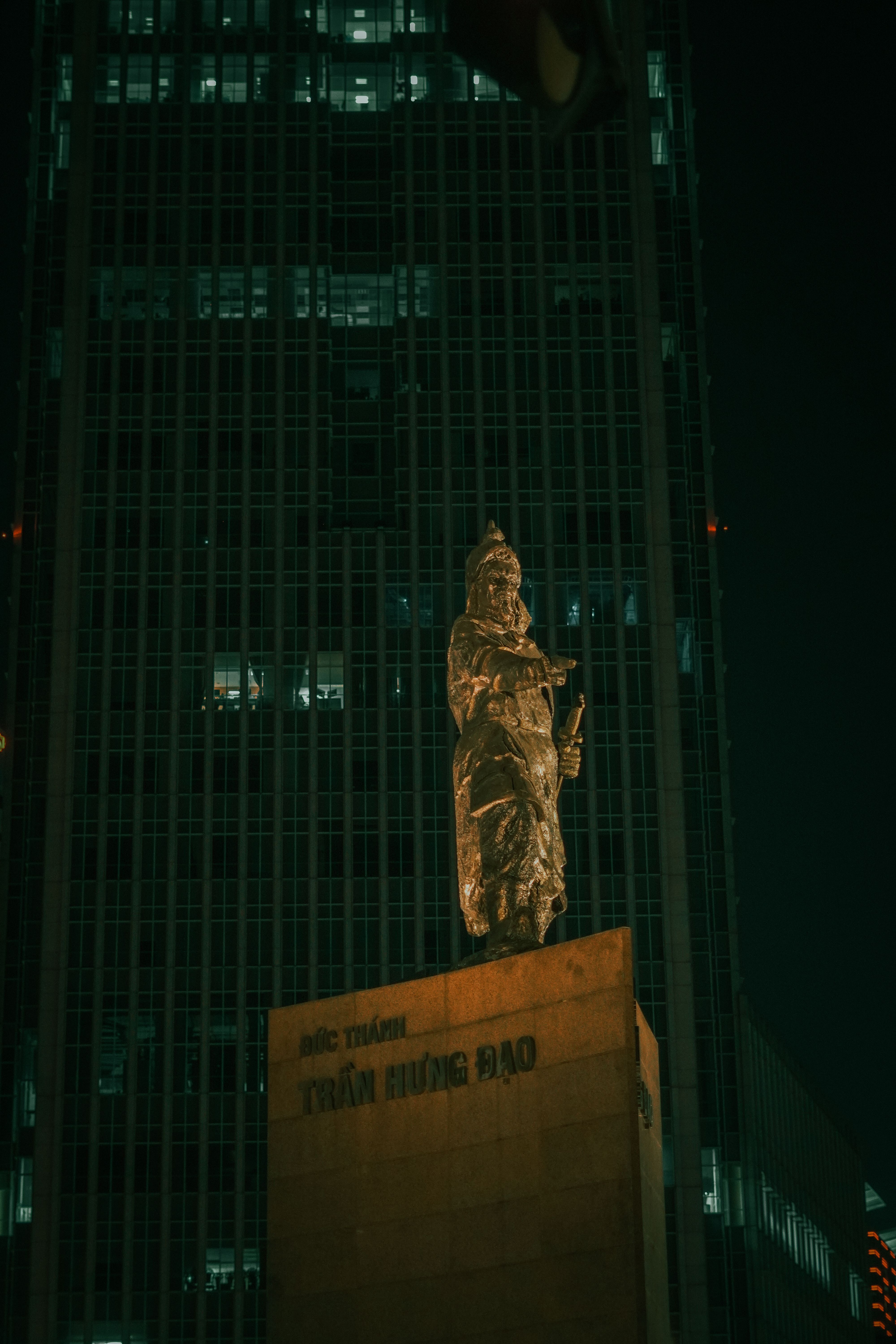 Majestic statue illuminated against a towering skyscraper at night in an urban setting.