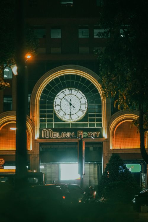 Free Urban street scene with illuminated clock tower and silhouettes of trees and cars at night. Stock Photo