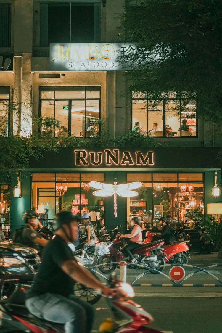 People Riding Motor Scooters In Front Of A Seafood Restaurant