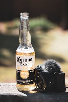 Corona beer bottle next to a camera with microphone outdoors. Perfect for beverage and photography themes.