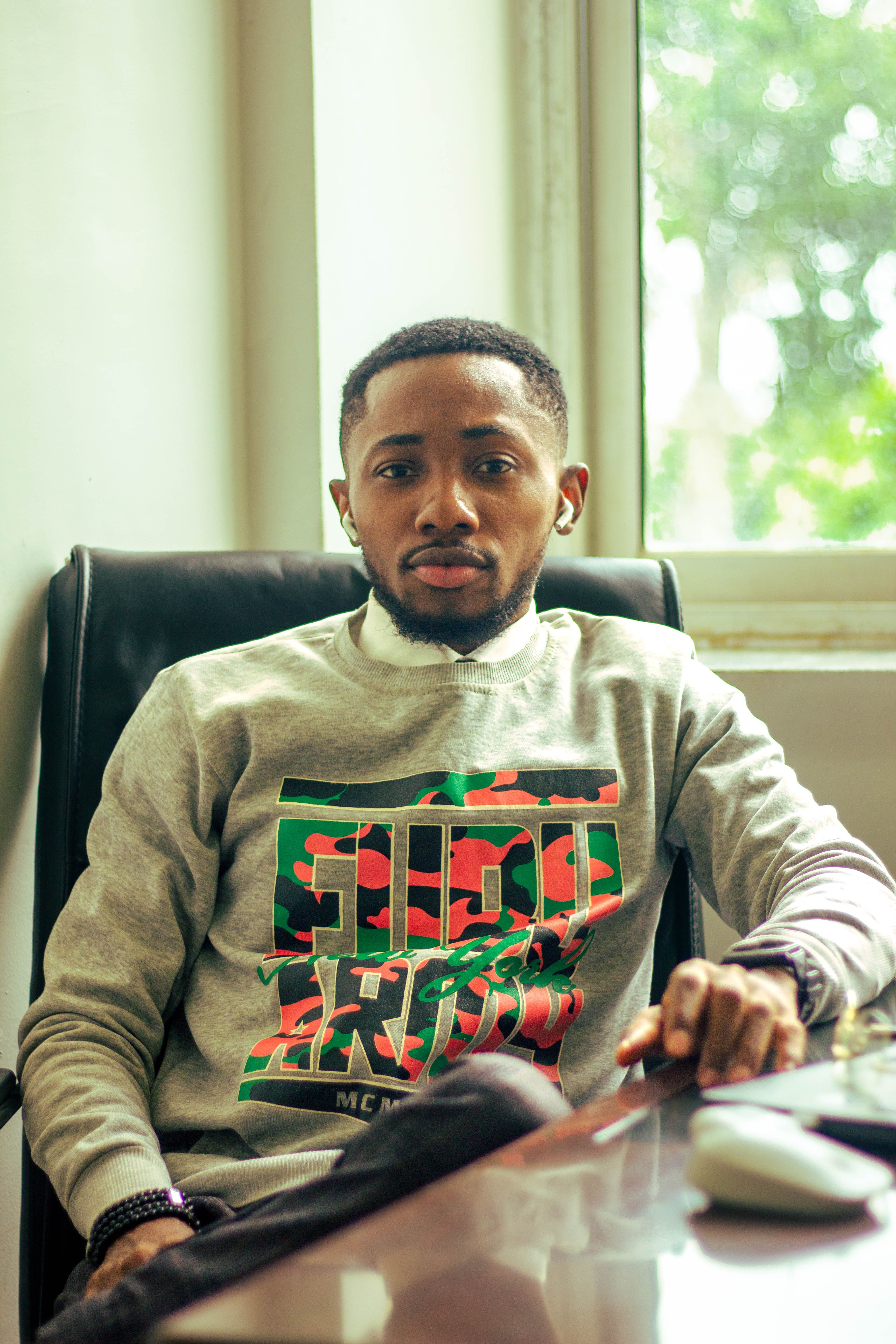 Portrait of a young man in smart casual outfit sitting by a window at a desk.