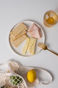 Flat lay of cheese, crackers, ham, and lemon on a white background.