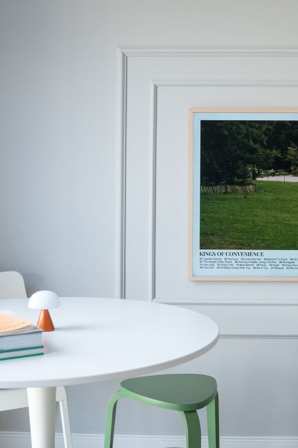 Elegant home interior with round white table, green stool, and wall art. Bright and modern aesthetic.