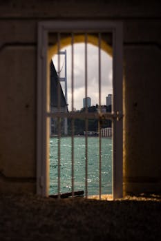 A scenic view of the Bosphorus Bridge through an iron gate, capturing the sea and city skyline.