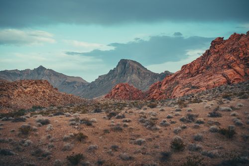 Free Mesmerizing view of a rugged desert landscape, featuring striking red rock mountains under a moody sky. Stock Photo