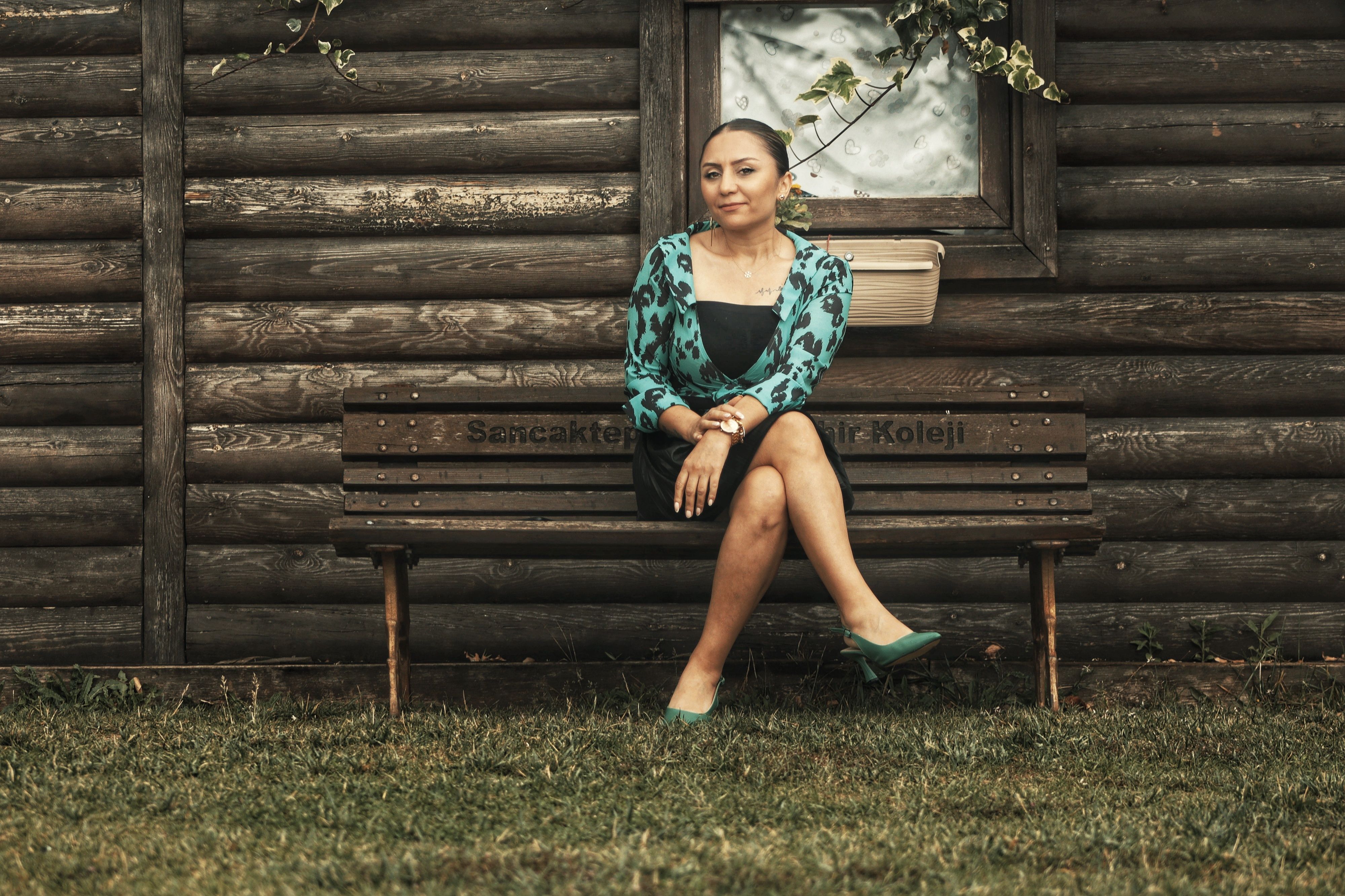 Elegant woman posing on a bench with a rustic wooden backdrop, exuding sophistication.