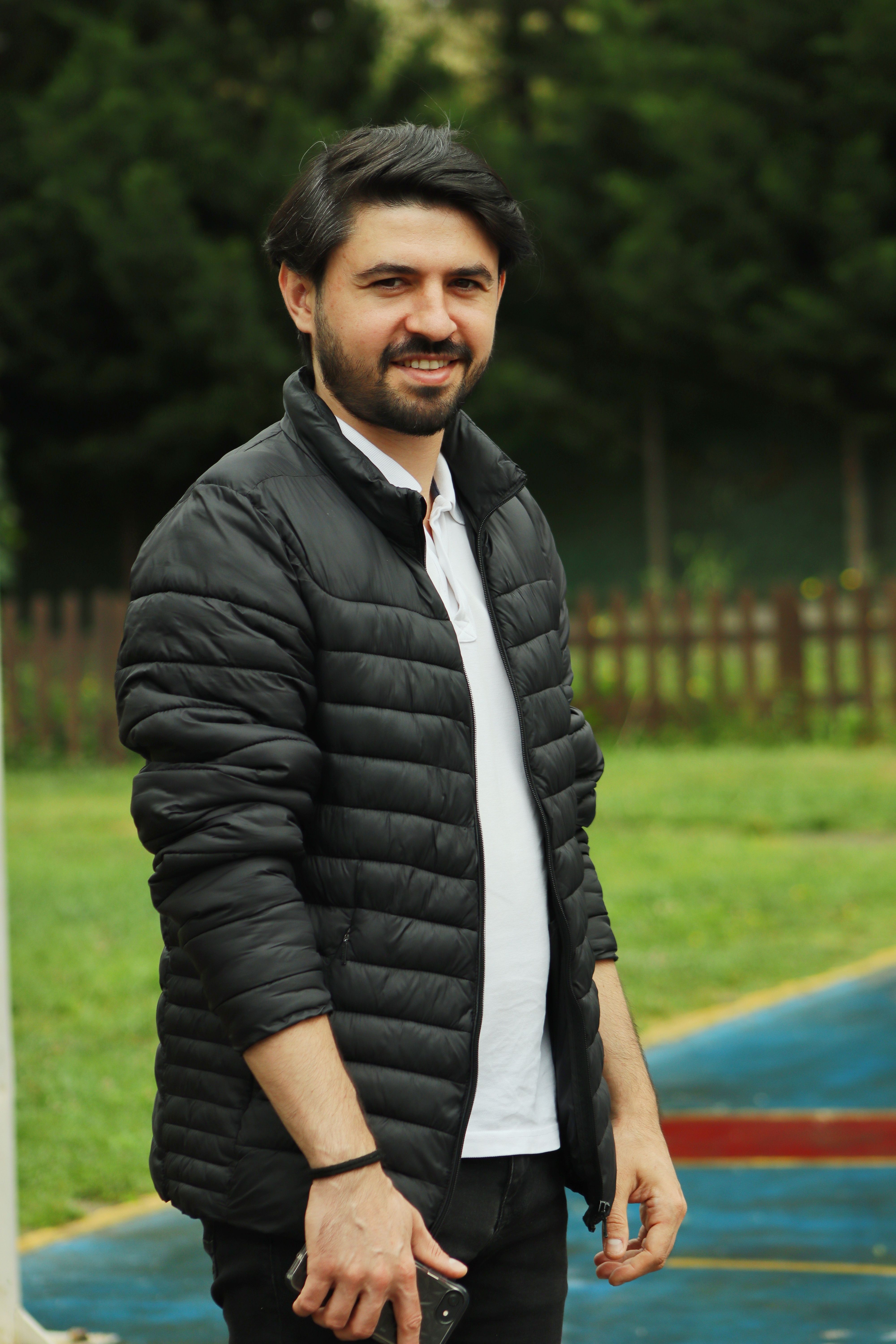 Stylish man posing outdoors in a black jacket with a natural background.