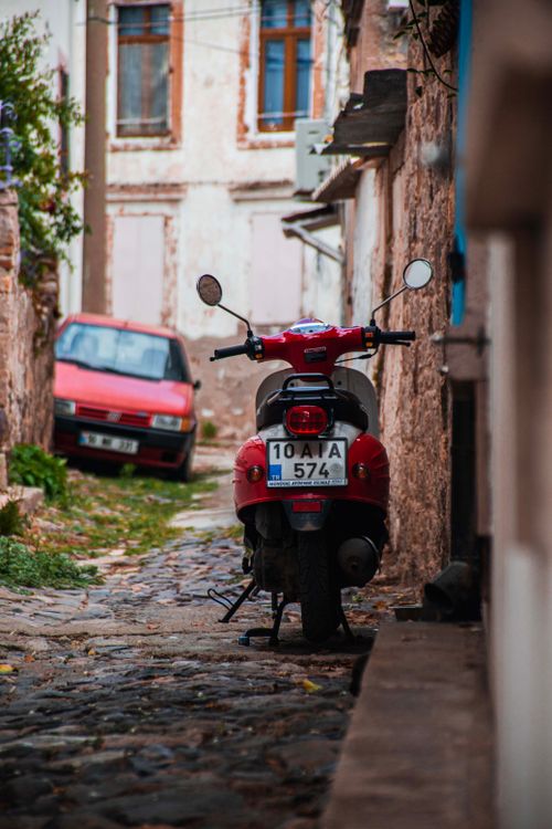 Free Vintage motorcycle and car in a rustic alleyway of Ayvalık, exuding old-world charm. Stock Photo