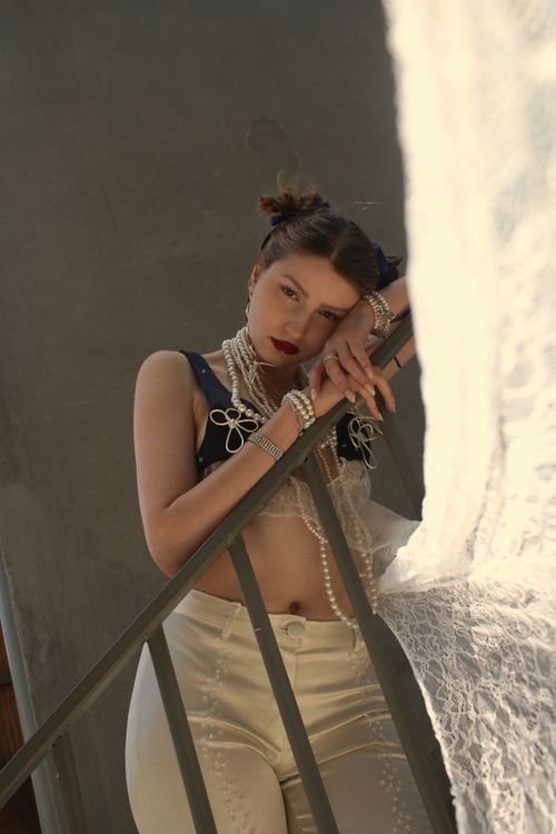 Free Chic portrait of a woman in braided hair with pearls, leaning gracefully on a handrail indoors. Stock Photo