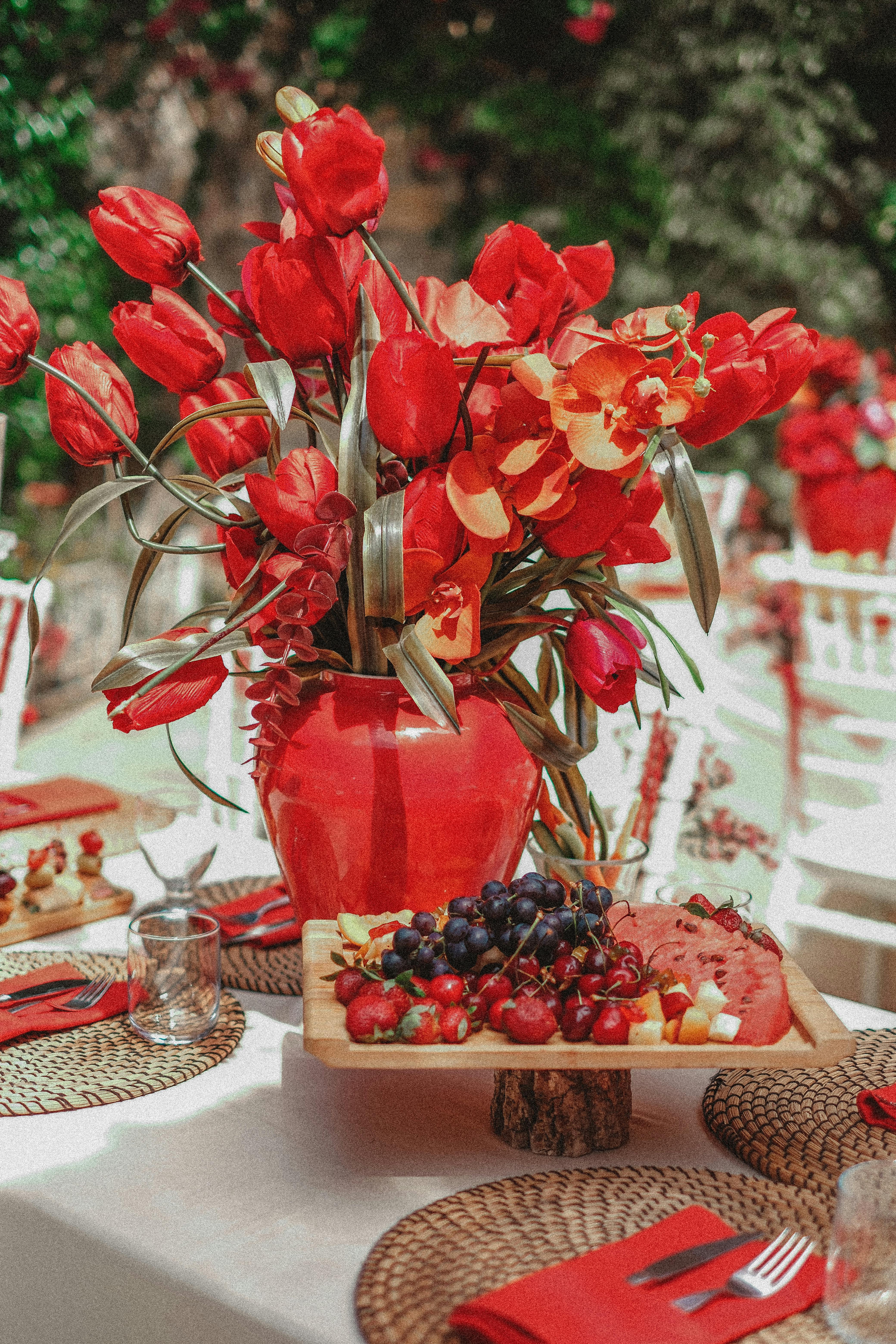 A vibrant floral arrangement with red tulips and a colorful fruit platter on an outdoor dining table.
