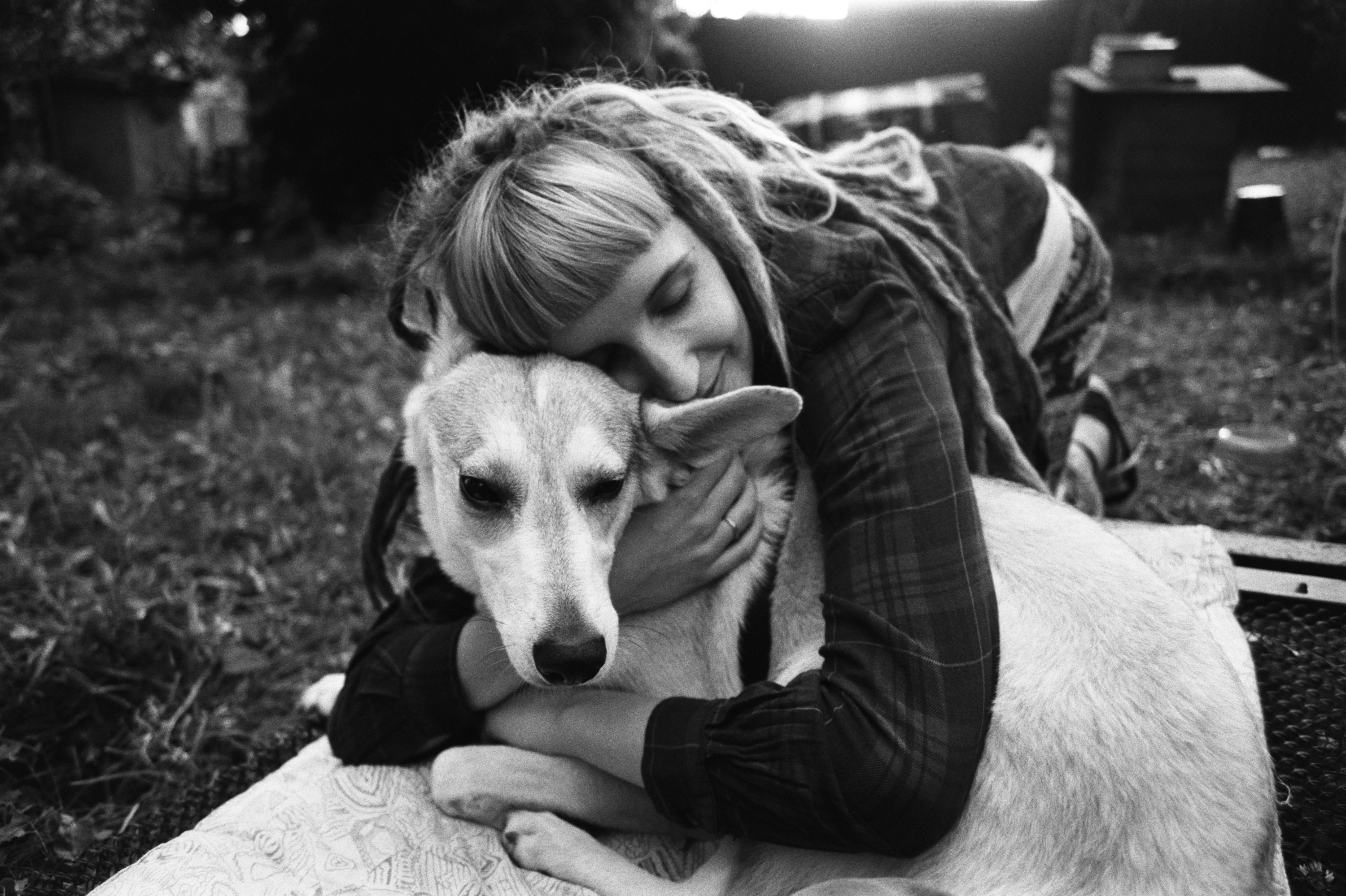 A woman lovingly embraces her dog outdoors in a park, captured in monochrome.