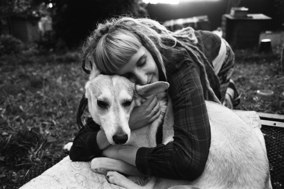 A woman lovingly embraces her dog outdoors in a park, captured in monochrome.