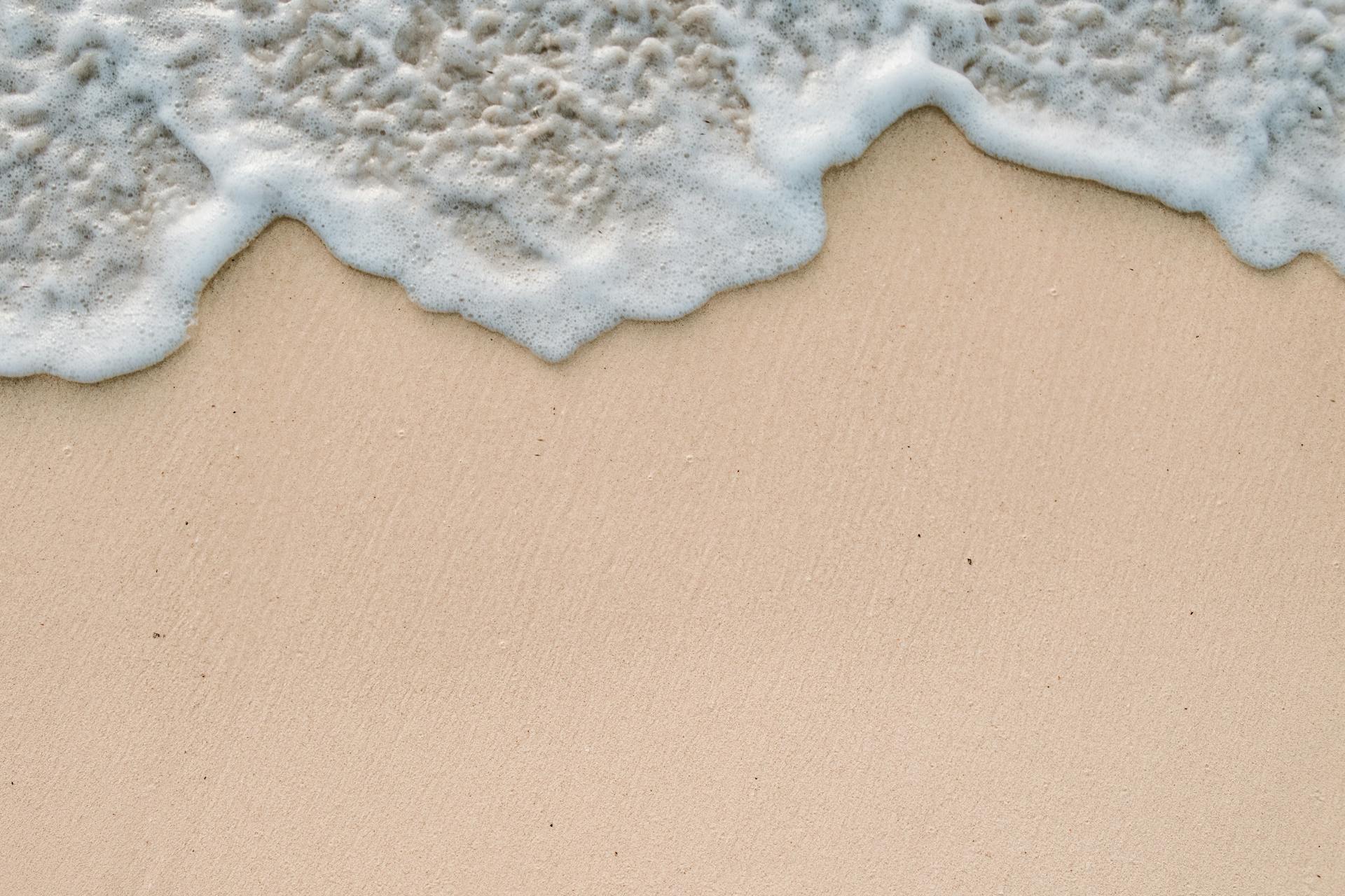 Close-up of a sandy beach with gentle ocean waves and foam, capturing a peaceful shoreline scene.