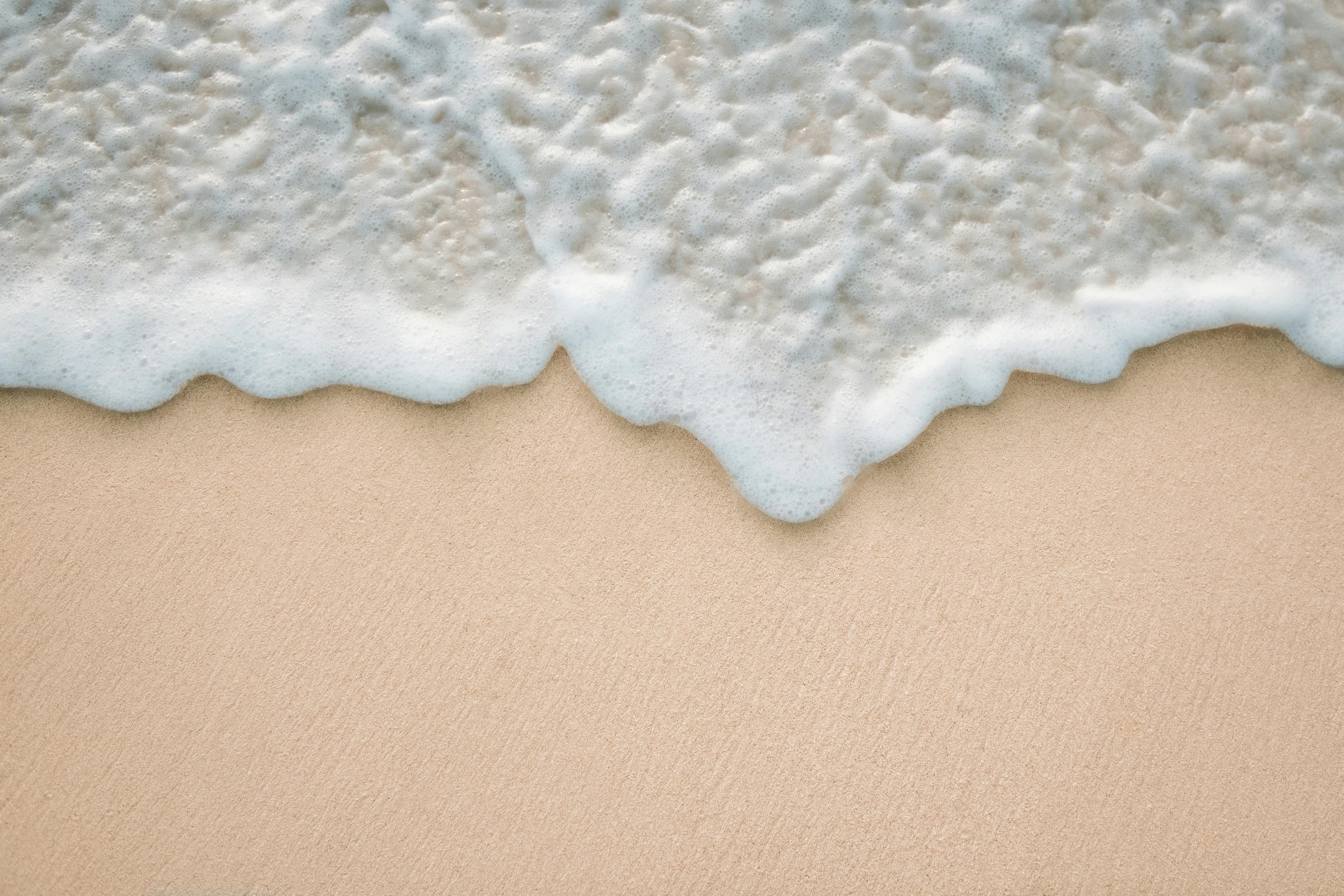 Calming sandy beach with soft waves and foamy water, shot from above.