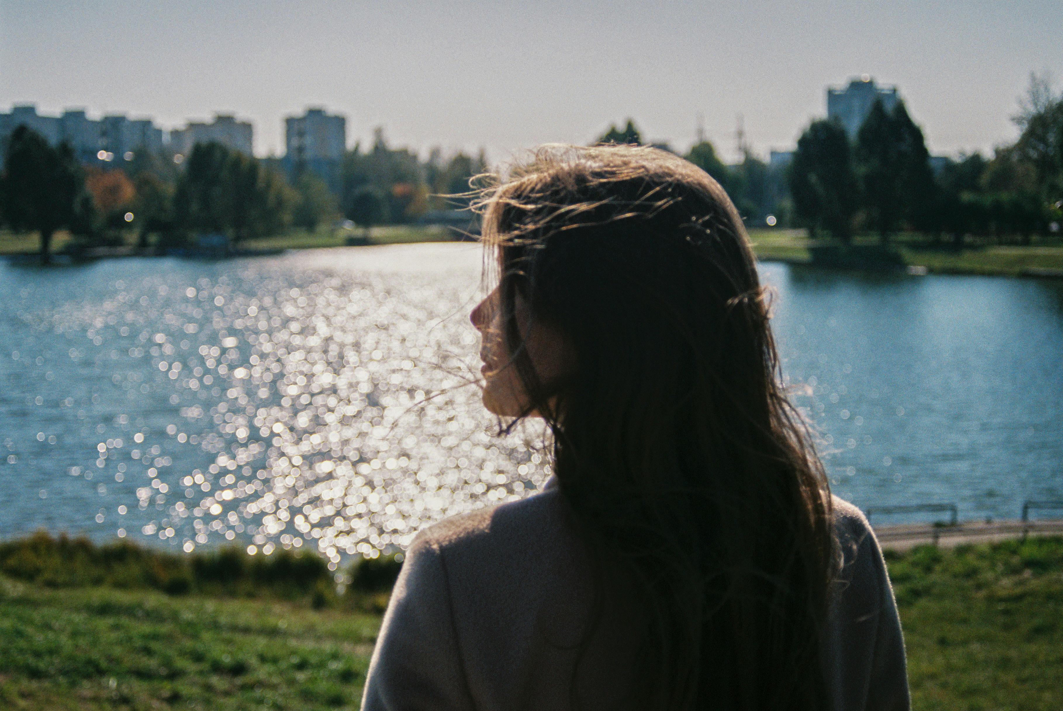 A serene moment of a woman overlooking a sunlit pond in an urban park, capturing tranquility and nature.