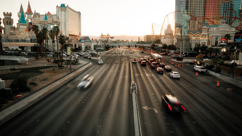 Vehicles moving along a Las Vegas resort corridor street at night with hotel lights overhead