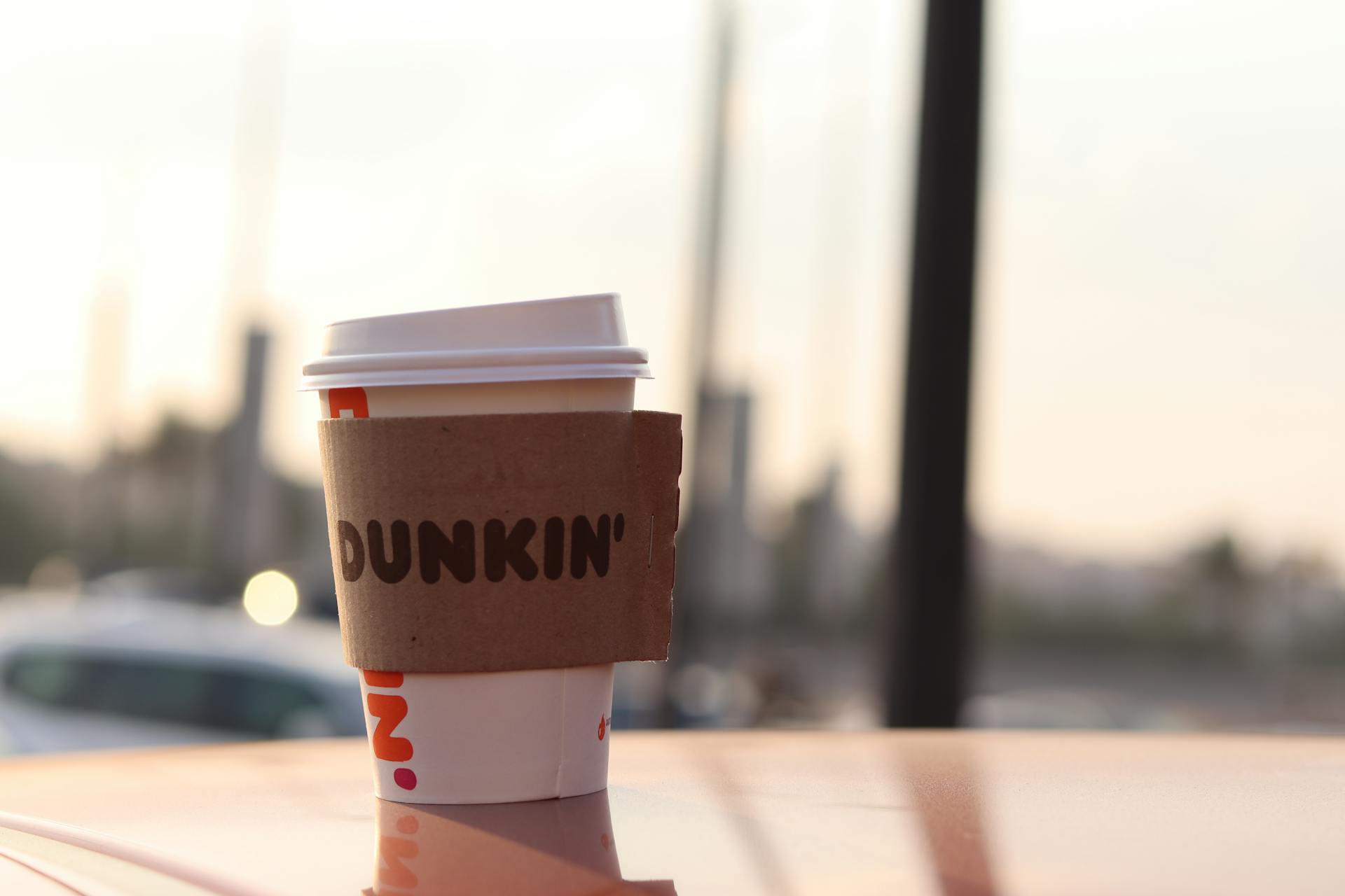 A Dunkin' coffee cup stands outdoors on a surface, captured in soft evening light.