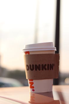 Takeaway Dunkin' coffee cup with sleeve outdoors in warm light, perfect for caffeine lovers.