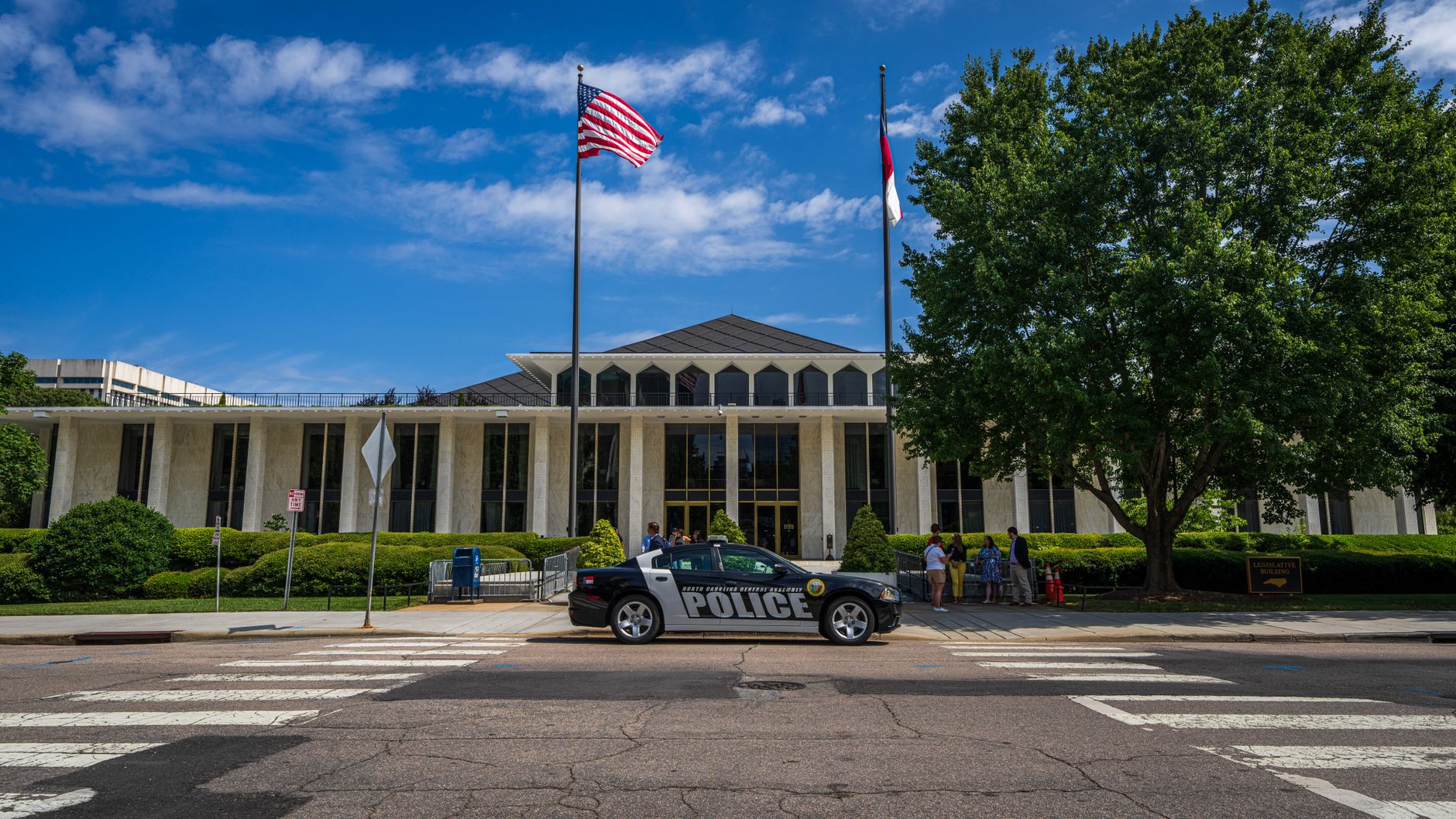 Government building facade with flags and police car in front on a sunny day.