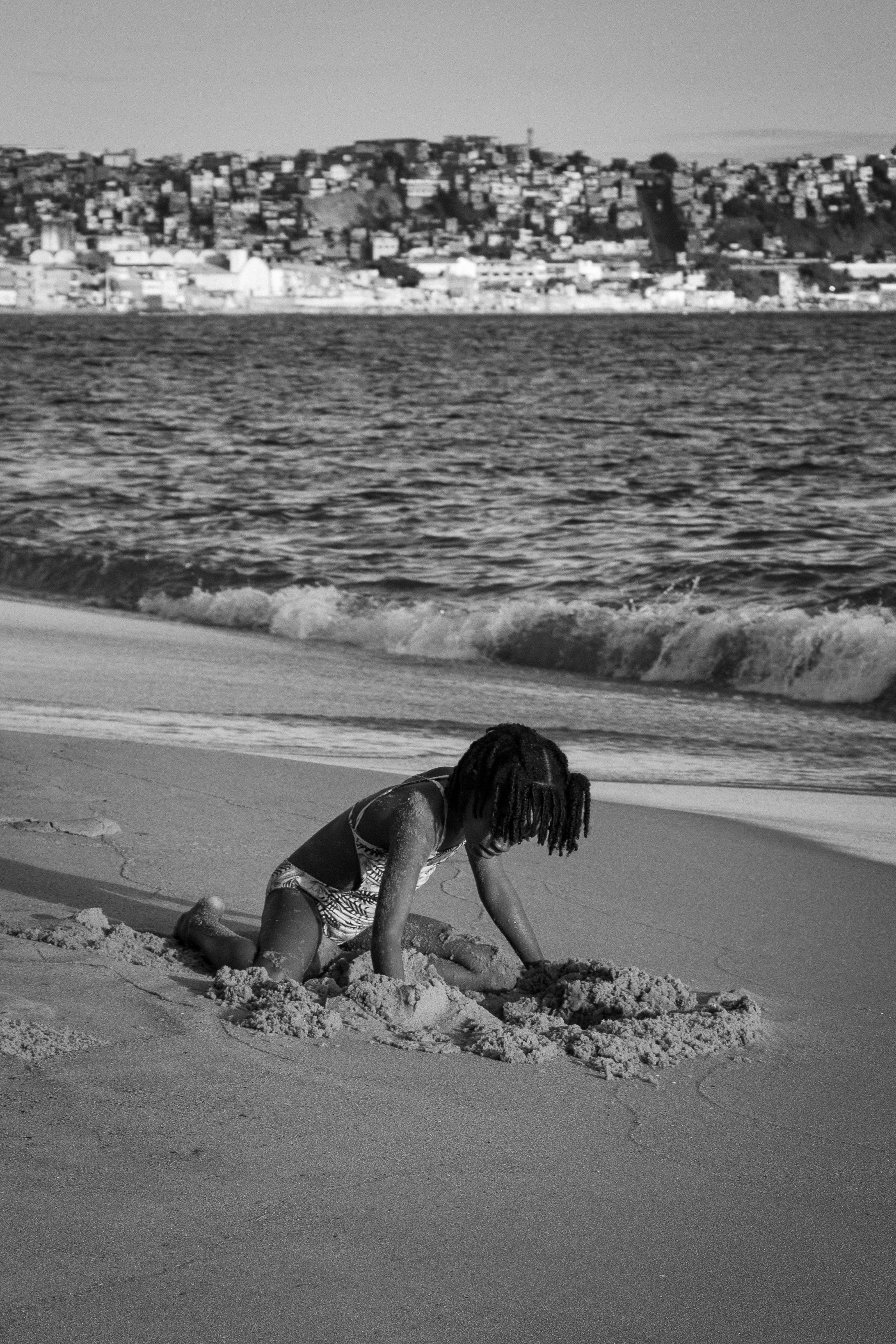 A child enjoys playing in the sand on a sunny beach day captured in black and white.