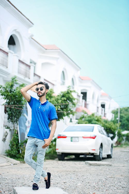 Man in Blue Shirt Holding His Hair Standing on Concrete Slab