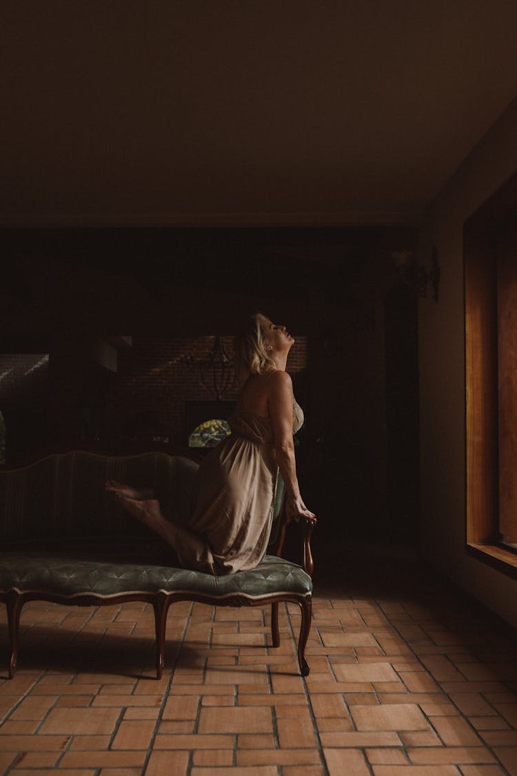 Woman In Dress Kneeling And Posing On Couch In Room