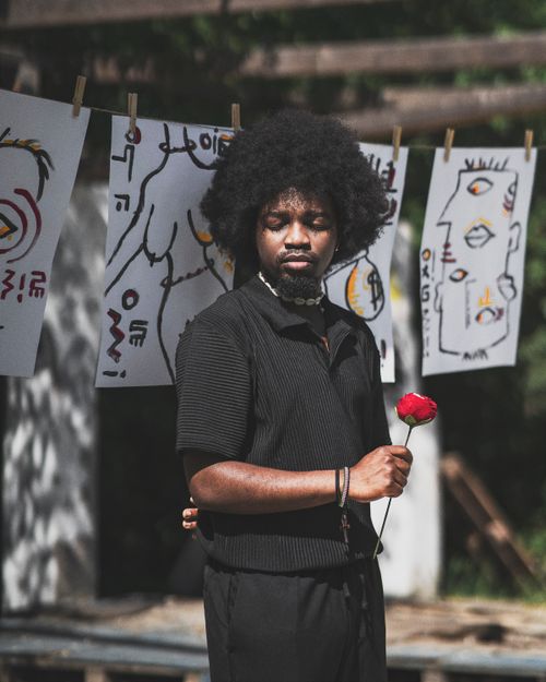 Free Fashionable man with Afro hair holding a red rose in an artistic outdoor setting. Stock Photo