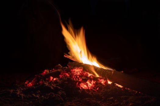 A close-up shot of a campfire with glowing embers, flickering flames set against a dark night backdrop.
