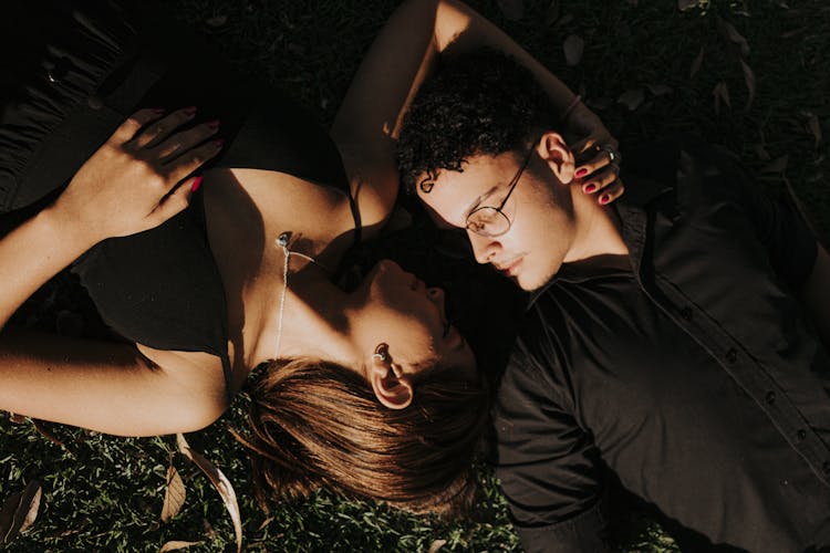 Young Couple Lying On Grass And Looking At Each Other 