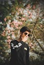 一名年轻人在户外盛开的树旁戴着太阳镜摆姿势，拍摄时尚照片