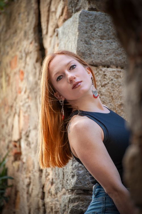 Free Stylish redhead woman posing against a rustic stone wall, embracing natural textures. Stock Photo