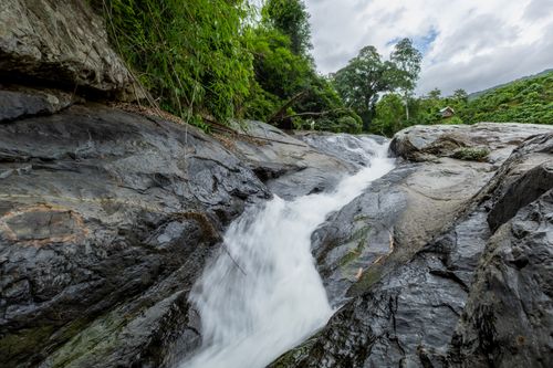 Free A tranquil waterfall cascading over rocks surrounded by lush greenery. Stock Photo