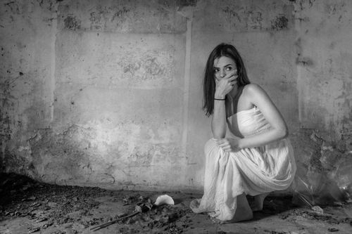Free A woman in a white dress sits thoughtfully in an abandoned room, highlighting decay. Stock Photo