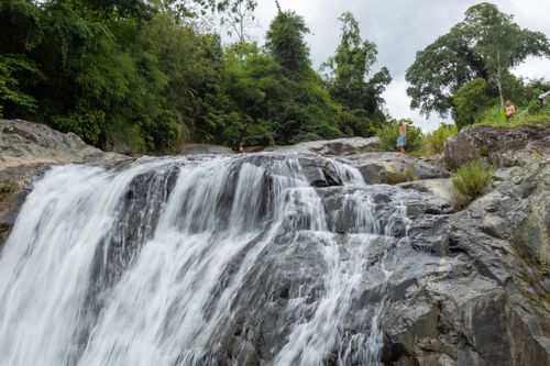 Free Beautiful waterfall cascading over rocks surrounded by dense green forest with people enjoying the view. Stock Photo