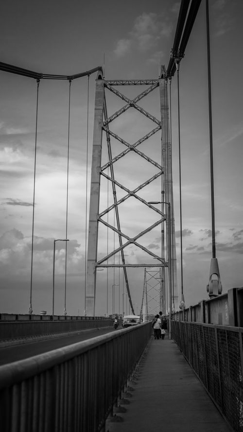 Free Black and white view of a suspension bridge with people walking, showcasing urban architecture. Stock Photo