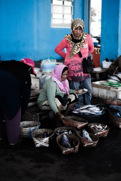 Free Women vendors at an outdoor market selling fresh fish in woven baskets. Stock Photo