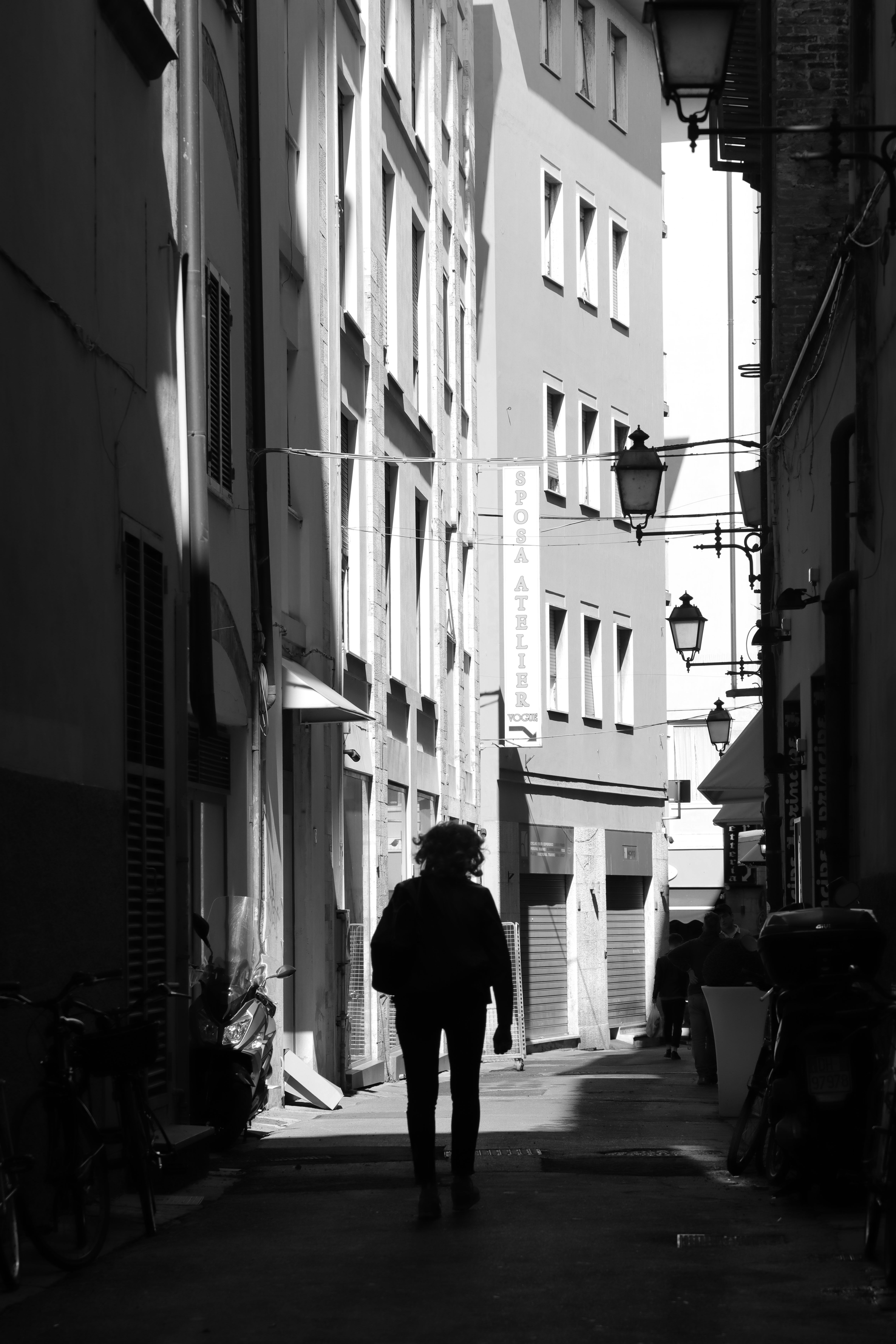 A black and white image of a person walking through a narrow alley in Florence, Italy.