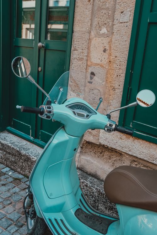 Free Retro-style blue scooter parked by a green door on a cobblestone street. Stock Photo