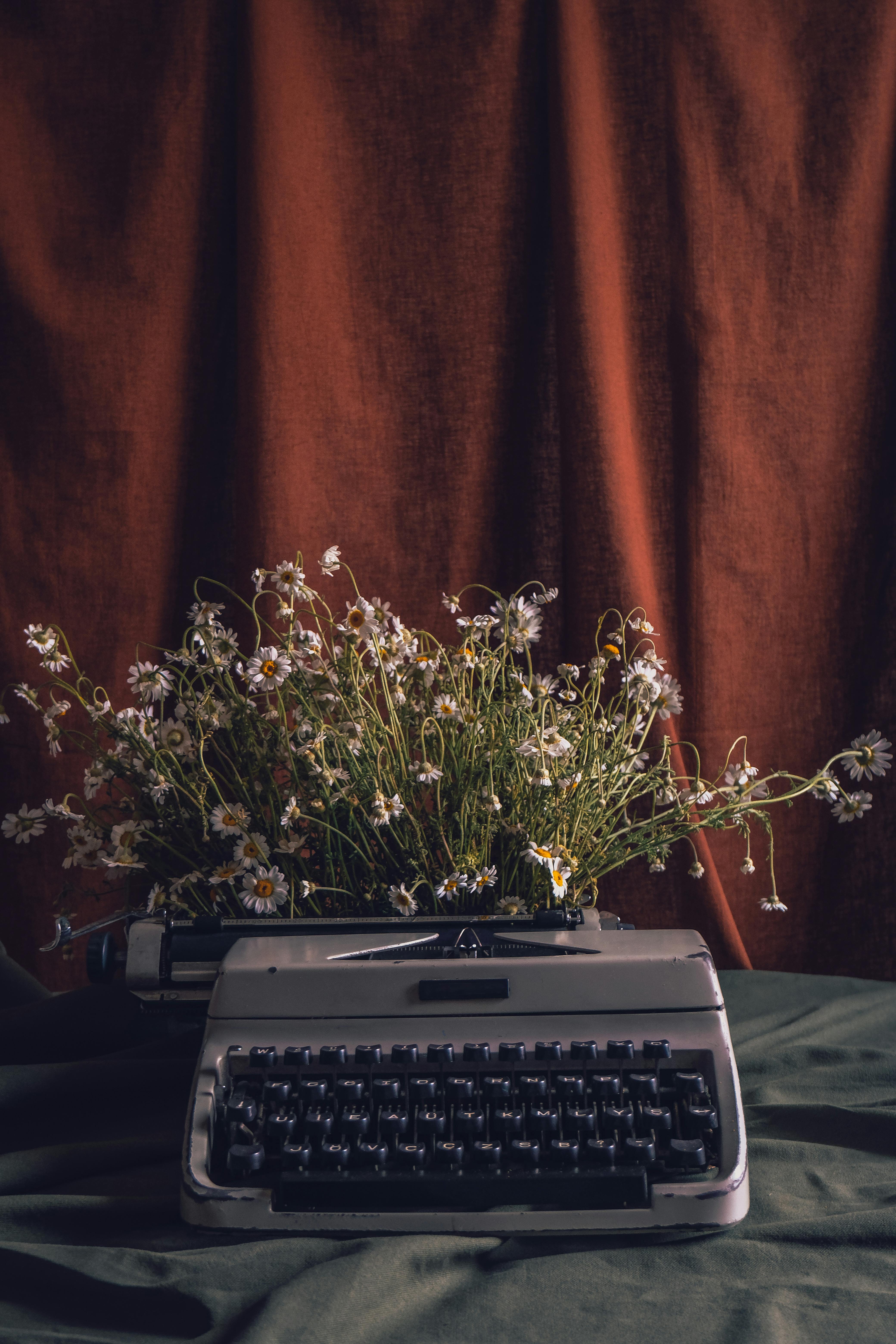 A vintage typewriter adorned with daisies against a rustic background, creating a retro still life scene.