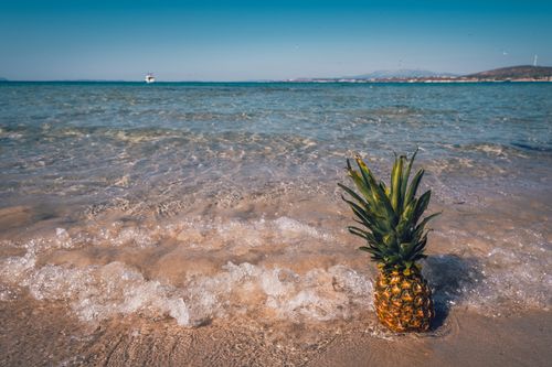 Free A pineapple sits on a sandy beach with waves in the background, capturing a tropical vibe. Stock Photo