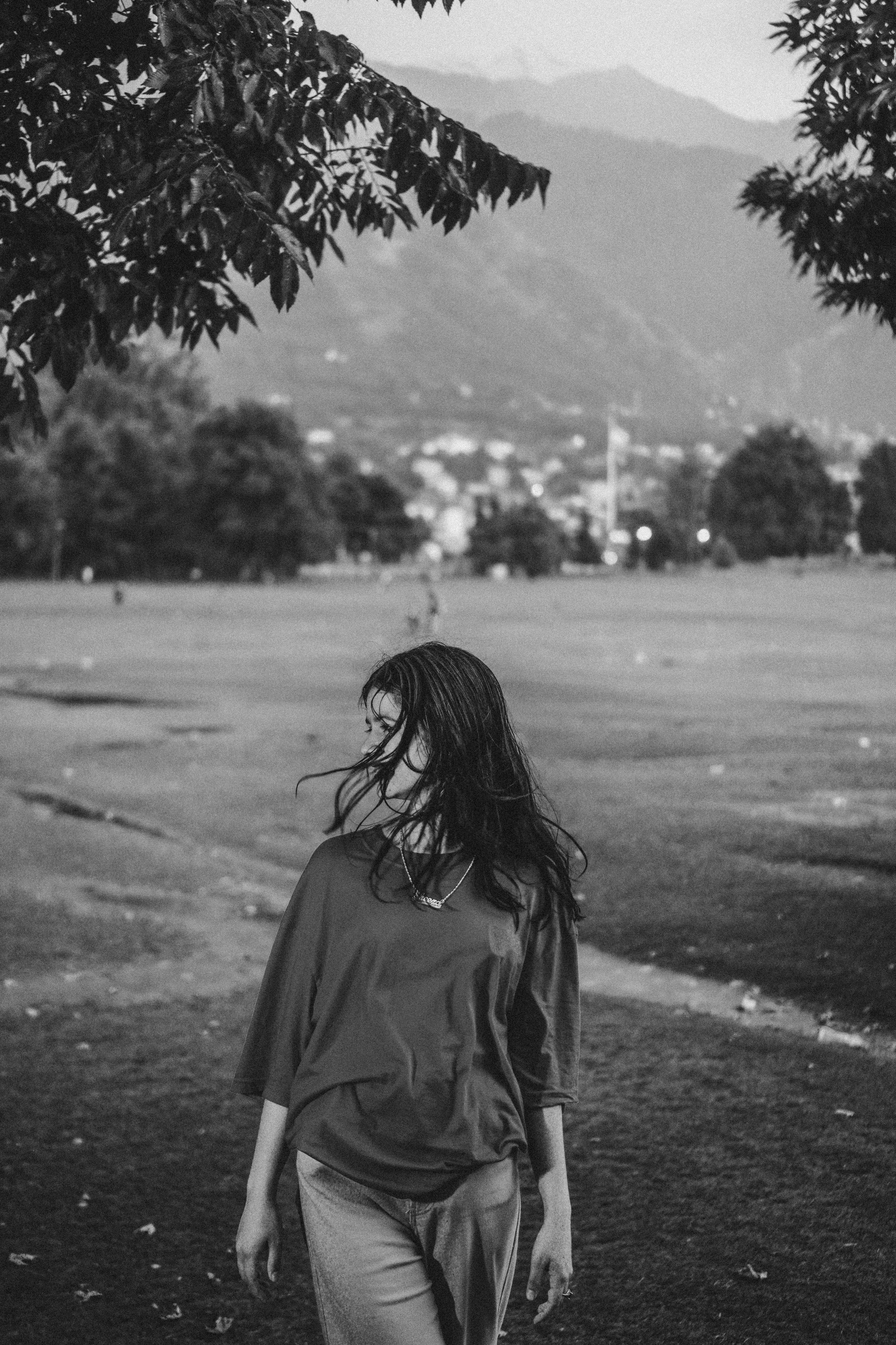 A young woman in a black and white portrait, standing in a serene field with mountains in background.