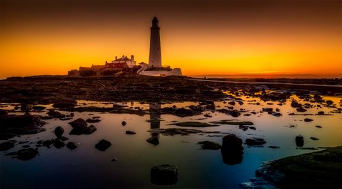 Free Dramatic sunset view of lighthouse reflecting in calm waters, evoking tranquility. Stock Photo