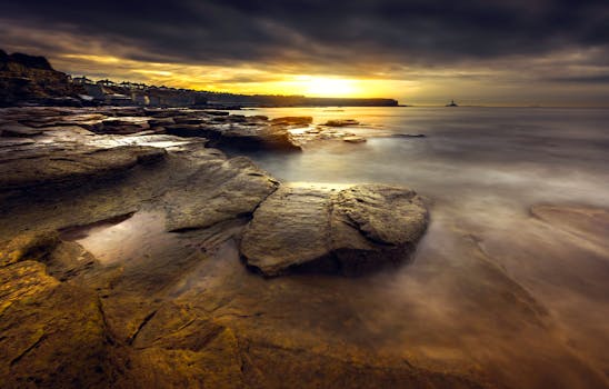 A stunning seascape at sunrise featuring a rocky shoreline and a dramatic sky.