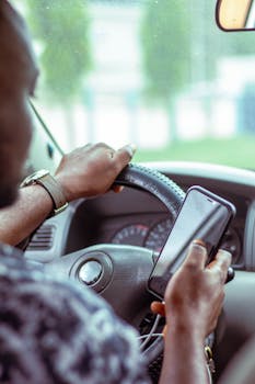 Close-up of a person using a smartphone while driving, focusing on hands and steering wheel.