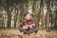 一名年轻人坐在森林里，弹着尤克里里，享受着轻松而艺术的时刻