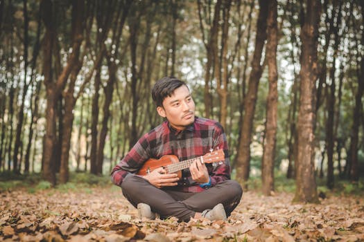 一名年轻人坐在森林里，弹着尤克里里，享受着轻松而艺术的时刻
